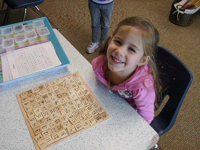 A young girl, smiling in front of a grid of numbers from 1 to 100.